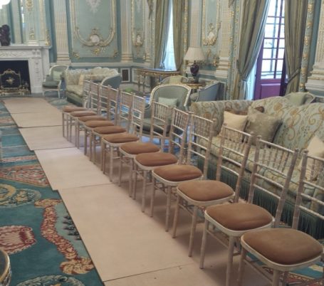 Long row of chairs in a grand ballroom, with MDF sheets on the floor being measured for makeshift tabletops.