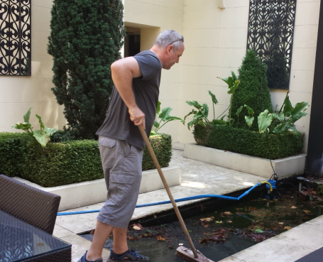 Craig sweeping debris from a water feature in a neatly landscaped courtyard.