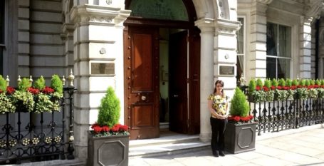 Kirsten standing at the entrance of the mansion with floral displays outside.